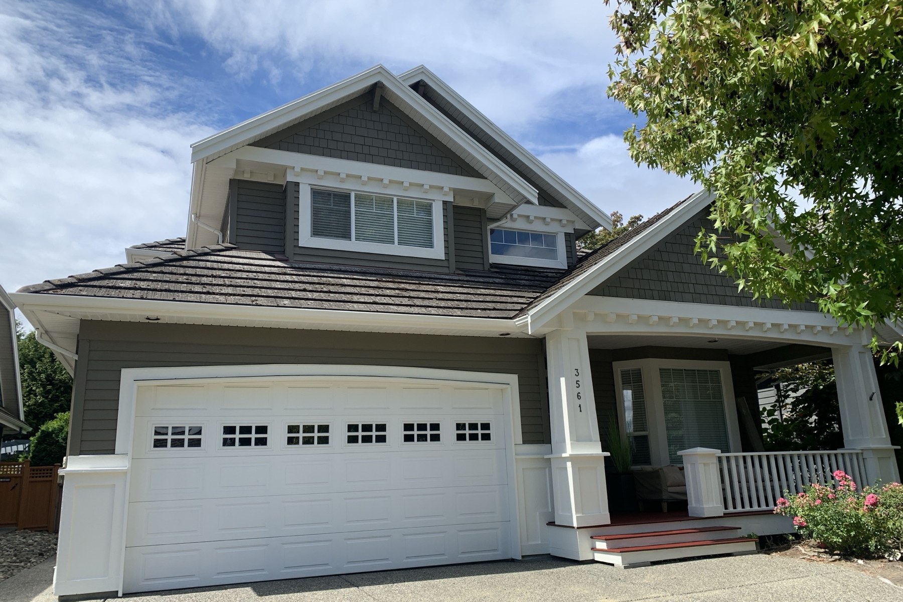 A craftsman house after repainting by Thompson Painting — deep warm grey siding, bright white trim and freshly stained red porch steps