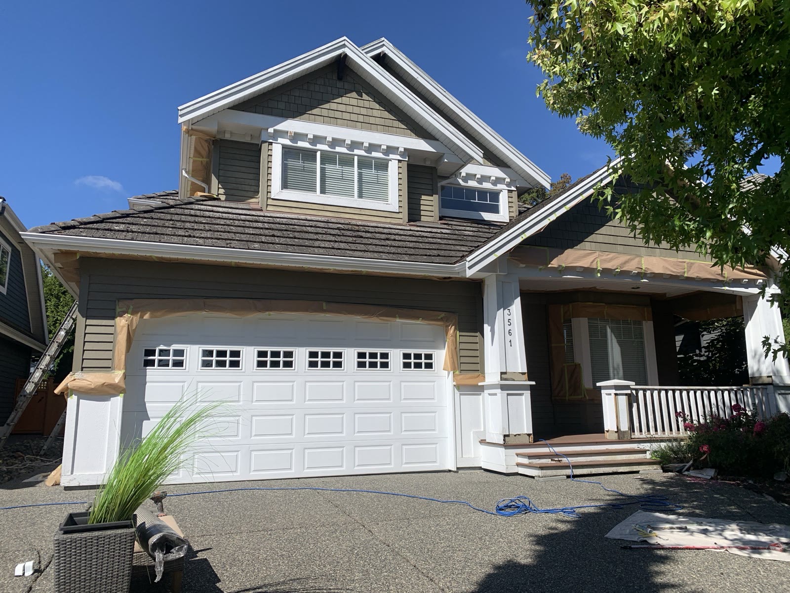A craftsman house mid-repaint, garage door, windows and porch fully masked with paper and tape before spraying