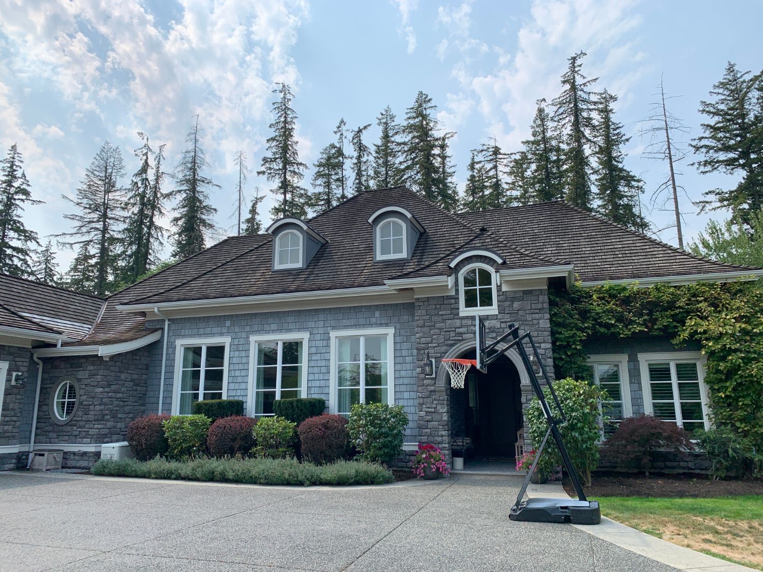 A large grey stone-and-shake house freshly painted by Thompson Painting — arched entry, white trim and dormers, tall evergreens behind